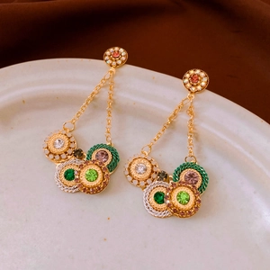 Close-up of vintage golden fringe earrings with colorful rhinestones on a ceramic tray