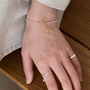 Close-up of heart charm bracelet and minimalist silver rings on hand in warm natural light