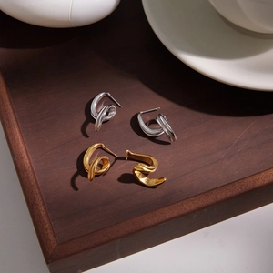 Detailed shot of twisted 18K gold and silver steel earrings on a wooden tray