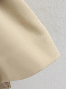 Close-up of beige trench coat fabric showing tight plain weave and detailed stitching