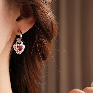 Close-up of silver heart earring with red gemstone and vintage texture on model