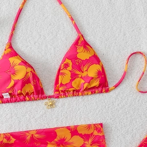 Detail of tropical floral print bikini with a gold flower charm on white faux fur background
