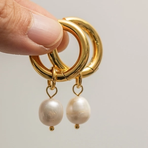 Close-up of hand holding gold hoop earrings with white freshwater pearl pendants