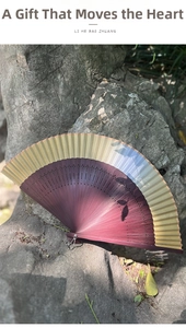 Detail of purple gradient folding fan with hollow carved bamboo and metal chain on rock