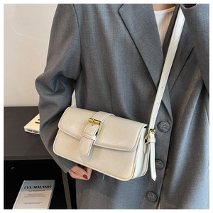 Detail of cream wax leather crossbody bag with golden buckle on grey suit background