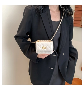 Close-up of a white quilted mini crossbody bag with a gold chain strap on a black blazer