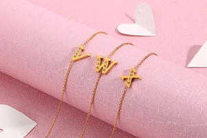 Detail of gold letter V W X pendants with zircon inlay on a pink decorative stand