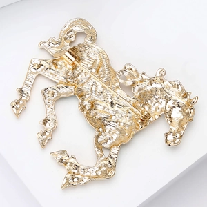 Macro detail of the golden horse brooch back showing the metal texture and pin fastener
