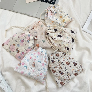 Detailed view of various cartoon embossed drawstring pouches on soft fabric bedding