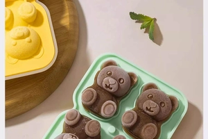 Detail view of yellow and green silicone bear ice cube molds on a wooden tray