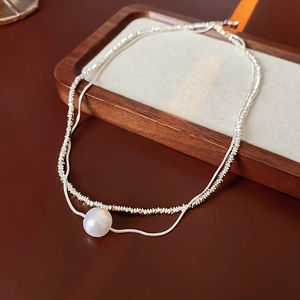 Détail du collier double rang argenté avec métal en forme de cœur et grande perle blanche