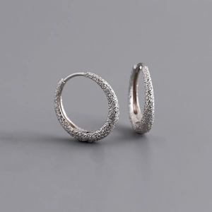 Close-up of silver hoop earrings with a textured sparkling sand finish on grey background