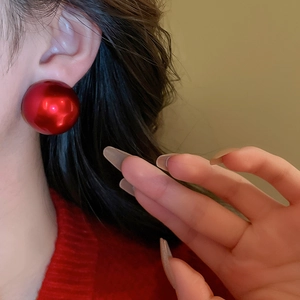 Close-up of elegant red round shell pearl earrings worn by a model in red knitwear