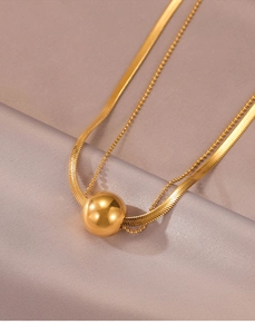 Detailed shot of double-layer gold necklace with snake chain and round bead pendant