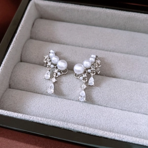 Close-up of pearl and zircon drop earrings resting on a grey velvet jewelry tray