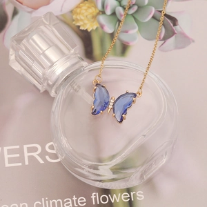 Elegant gold chain necklace with blue crystal butterfly pendant on decorative perfume bottle