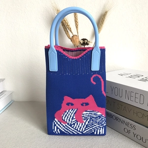 Detail of knitted mini handbag featuring a pink cat motif and blue soft rubber handle