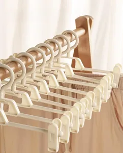 Close-up of adjustable beige plastic hangers with clips on a wooden closet rod