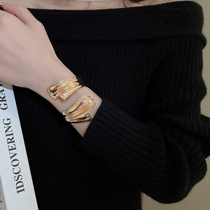 Nahaufnahme einer goldenen Wellenarmspange am Arm mit polierter metallischer Textur