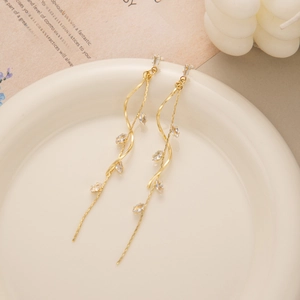 Close-up of elegant gold leaf tassel earrings with sparkling zircons on a white ceramic plate