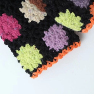 Close-up of handmade crochet cardigan featuring colorful floral motifs and orange borders