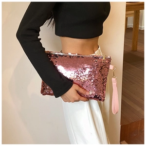 Detail of pink sequin mini clutch bag with gold zipper and wrist strap held by hand