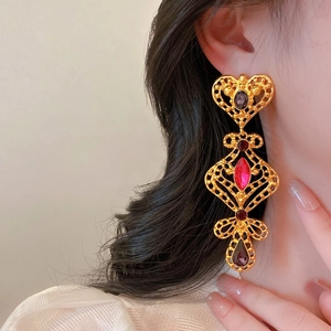 Dettaglio di orecchini vintage in oro con gemme rosse e nere indossati da modella