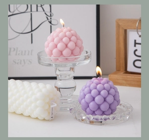 Artistic bubble-shaped scented candles in pink, purple and white on a glass holder