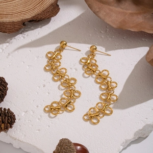 Vue détaillée de boucles d'oreilles trèfle dorées à pompons sur une surface en pierre