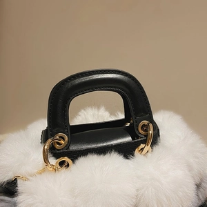 Detail of white plush fabric, black leather handle and gold metal ring on a handbag