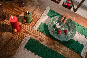 Close-up of green and cream woven placemat with tassels on a festive wooden table