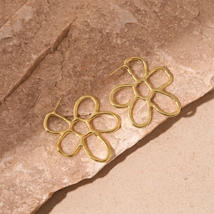 Macro detail of golden minimalist flower petal earrings on natural stone surface