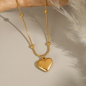 Collier avec pendentif cœur doré et chaîne à billes sur support bois fond neutre