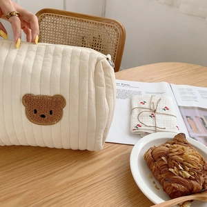 Detail of cream quilted cotton makeup bag with a soft plush bear embroidery on a desk