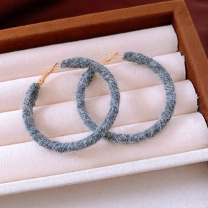 Close-up of gray wool hand-knitted round hoop earrings with fuzzy texture on velvet box