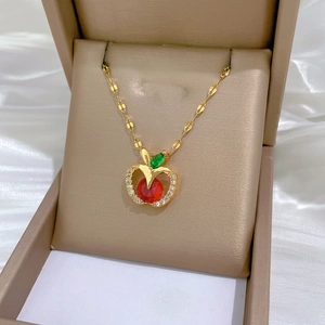 Gold apple necklace with red gemstone and diamonds displayed in a champagne jewelry box