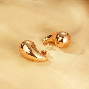 Macro detail of glossy gold-plated teardrop earrings on smooth beige silk fabric