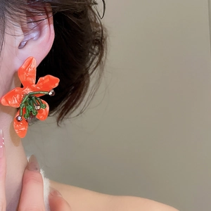 Close-up of large orange floral earring with green beads worn on a model's ear