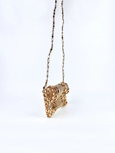 Detail of golden woven metal clutch bag featuring intricate beaded texture and chain strap