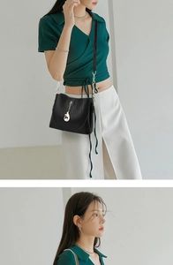 Detail of black leather crossbody bag with golden chain and fox charm on a model