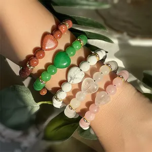 Detail of stacked natural stone bracelets featuring heart charms and crystal spacers on a wrist