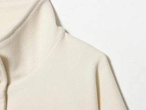 Detail of soft cream wool cape coat showing the stand collar and refined fabric texture