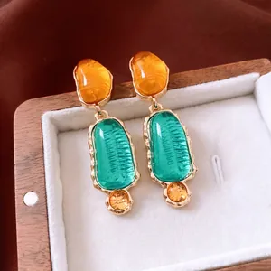 Vintage gold earrings with amber and emerald resin stones on a soft jewelry display