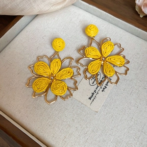 Detail view of yellow raffia woven flower earrings with golden metallic outlines