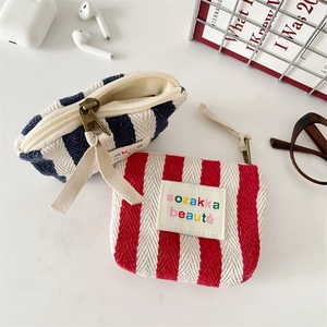Detail of striped canvas mini pouches with long zipper pulls and colorful logo labels