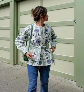 Detail view of a quilted floral jacket with blue patterns on white fabric and waist belt