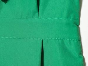 Close-up of green ruffle romper showing waist belt detail and high-quality double stitching