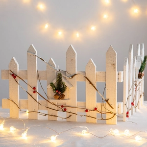 White wooden Christmas fence decoration with red berries, pine cones and warm LED lights