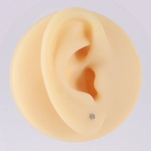 Close-up of a silver pentagram star earring on a silicone ear model for size reference