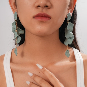Close-up of model wearing long tassel earrings with grey-green acrylic petals and gold chains